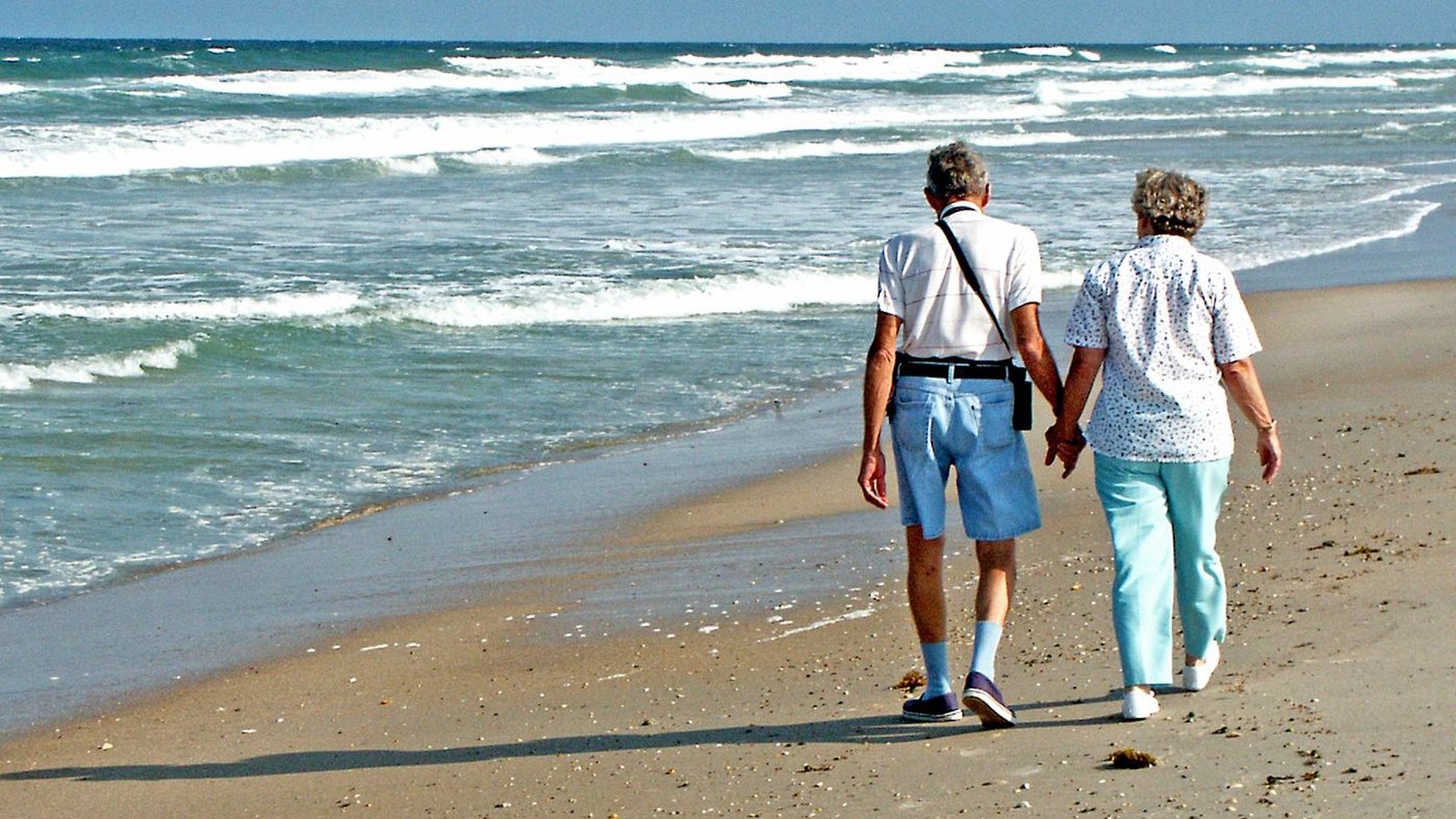 An older couple walking hand in hand along the shoreline