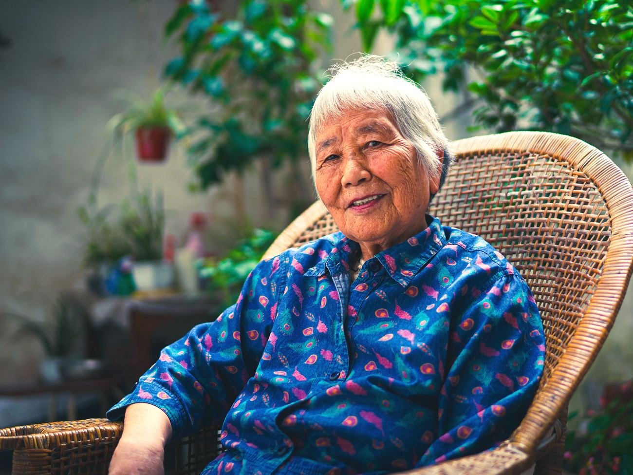 An older woman sitting among her plants at home